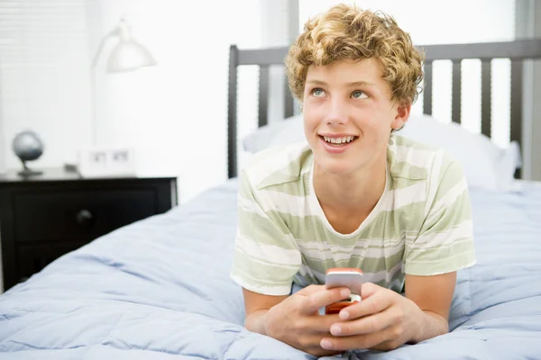 十几岁的男孩躺在床上使用的移动电话上 — 图库照片