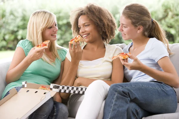 Девочки-подростки сидят на диване и едят пиццу вместе — стоковое фото