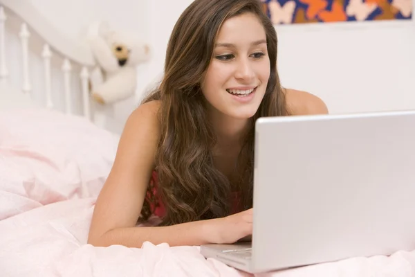 十几岁的女孩躺在她的床上使用笔记本电脑 — 图库照片