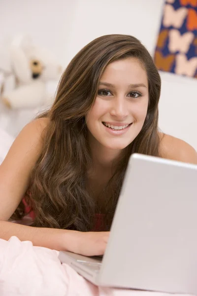 十几岁的女孩躺在她的床上使用笔记本电脑 — 图库照片