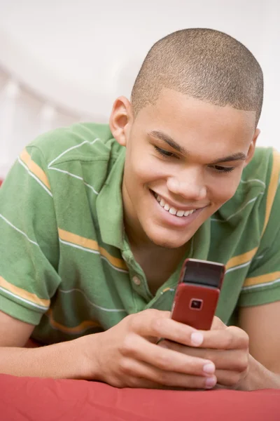 Dospívající chlapec leží na posteli pomocí mobilního telefonu — Stock fotografie