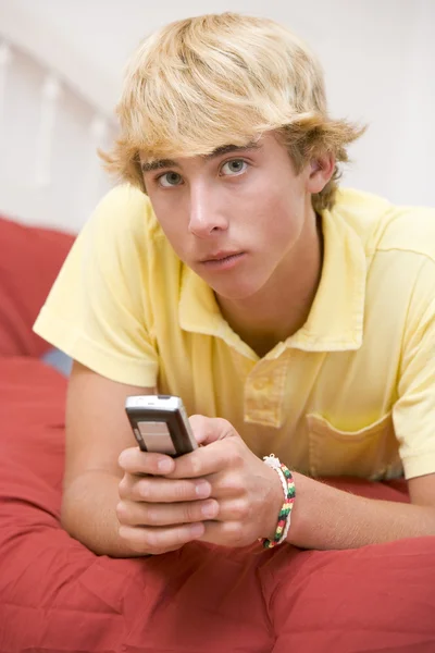 Dospívající chlapec leží na posteli pomocí mobilního telefonu — Stock fotografie
