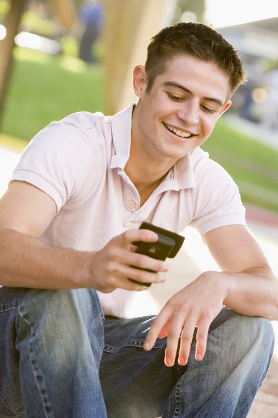 十几岁的男孩坐在户外使用的移动电话 — 图库照片