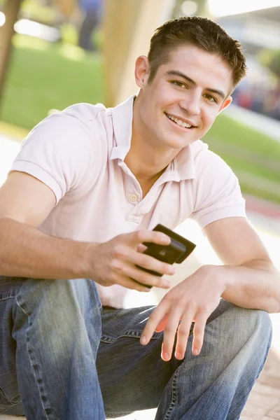 Nastoletni chłopiec siedzi na zewnątrz przy użyciu telefonu komórkowego — Zdjęcie stockowe