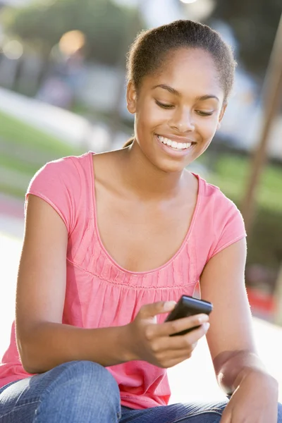 Adolescente niña sentada al aire libre utilizando el teléfono móvil —  Fotos de Stock