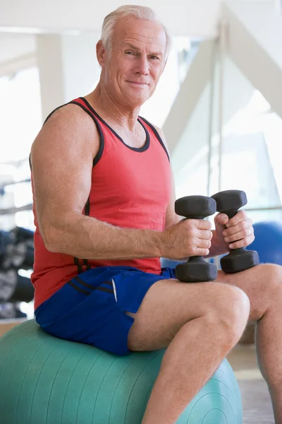 Homem usando pesos de mão na bola suíça no ginásio — Fotografia de Stock