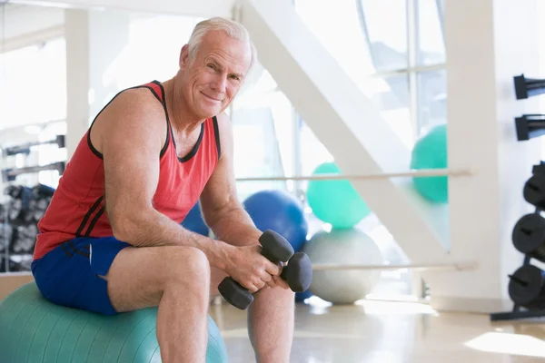 Mann mit Handgewichten auf Schweizer Ball im Fitnessstudio — Stockfoto