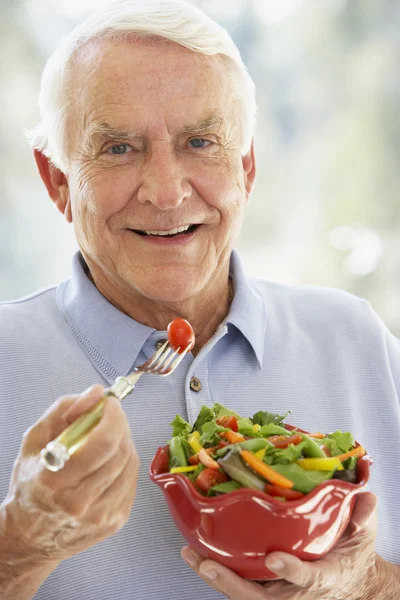 Hombre mayor sonriendo en la cámara y comiendo ensalada — Foto de Stock