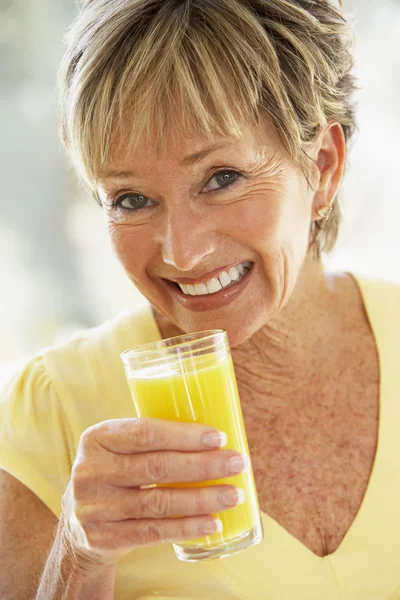 Mulher sorrindo na câmera bebendo suco de laranja — Fotografia de Stock