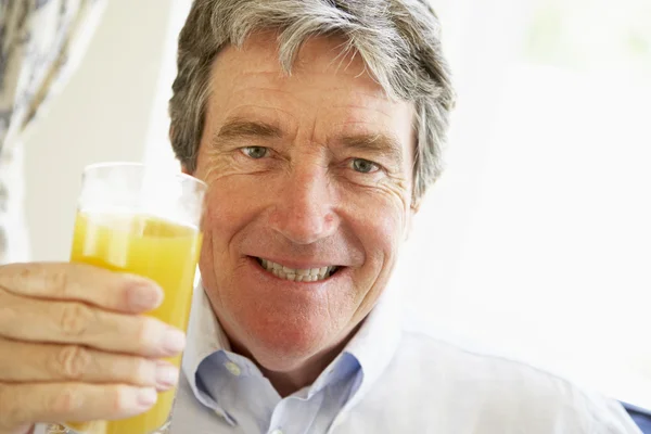 Senior man glimlachen op camera en drinken sinaasappelsap — Stockfoto