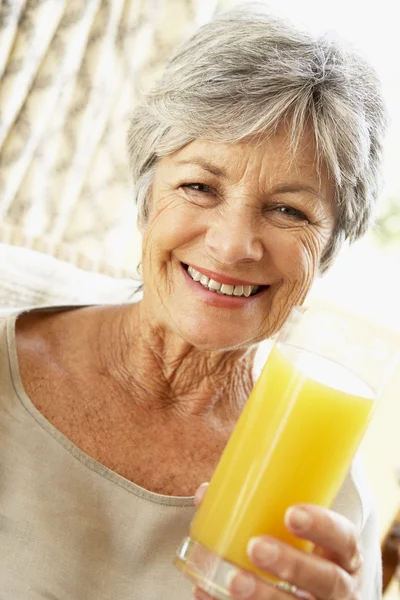 Старшая женщина улыбается перед камерой и пьет апельсиновый сок — стоковое фото