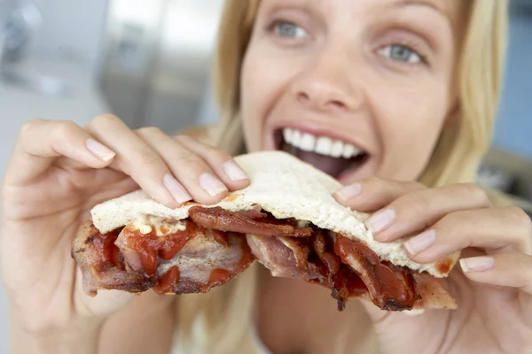 Женщина среднего возраста ест сэндвич с беконом — стоковое фото
