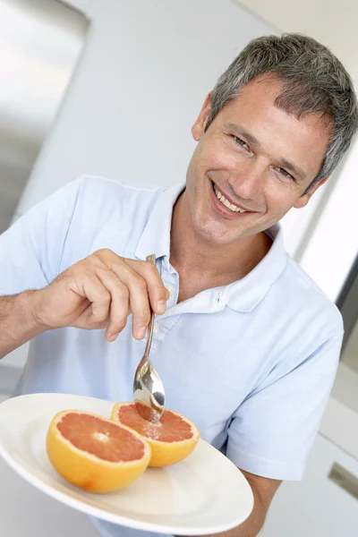Uomo di mezza età che mangia pompelmo fresco — Foto Stock