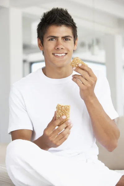 Jovem comendo um pão marrom rolo — Fotografia de Stock
