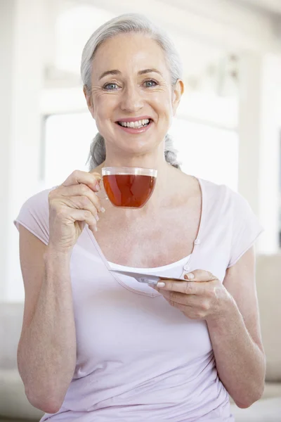 Старшая женщина держит чай и улыбается перед камерой — стоковое фото