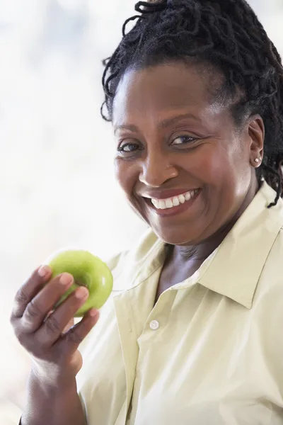 Старшая женщина ест зеленое яблоко и улыбается перед камерой — стоковое фото