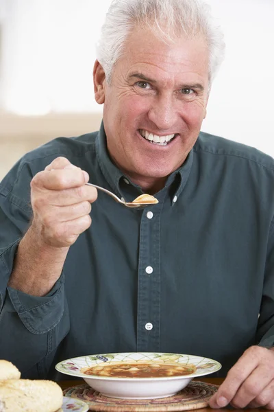 Старший человек ест суп, улыбается перед камерой — стоковое фото