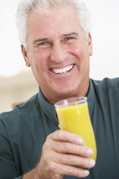 Uomo anziano che tiene un bicchiere di succo d'arancia fresco, sorridente al — Foto Stock