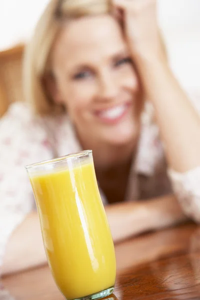 Mujer adulta mirando un vaso de jugo de naranja fresco — Foto de Stock