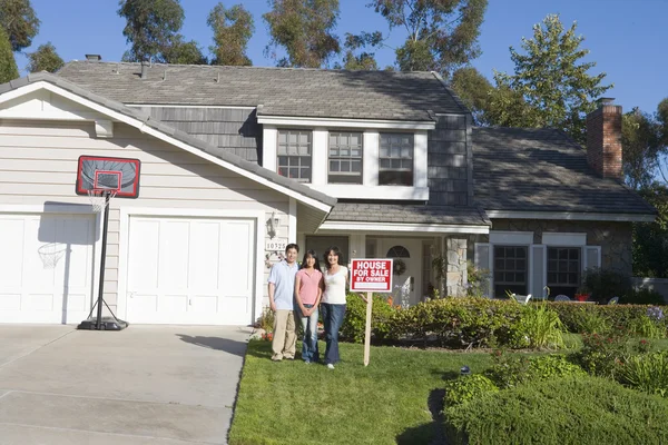 Familia de pie fuera de la casa con signo de bienes raíces — Foto de Stock