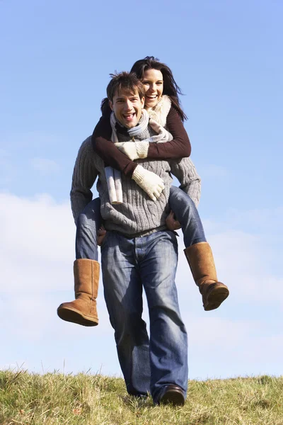 Człowiek daje jego żona piggy back ride w parku — Zdjęcie stockowe