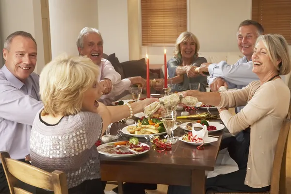 Amis tirant craquelins de Noël à une soirée dîner — Photo