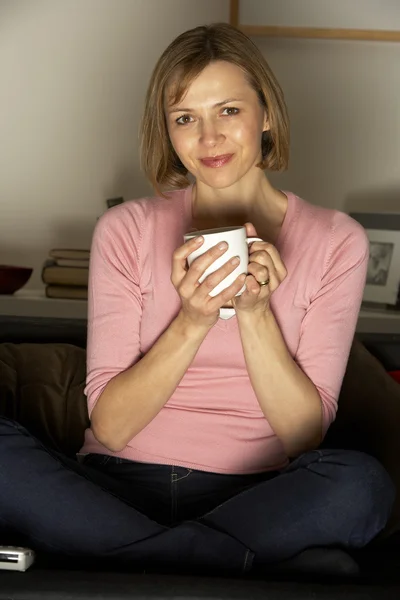 Женщина расслабляется за чашкой кофе, смотря телевизор — стоковое фото