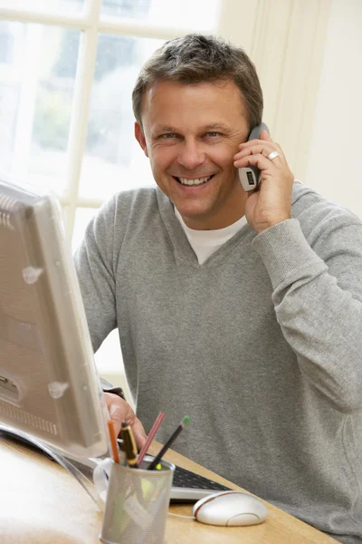 Человек, использующий компьютер и разговаривающий по телефону — стоковое фото