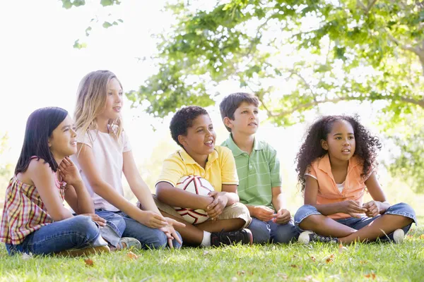 Five young friends sitting outdoors with soccer ball Stock Photo