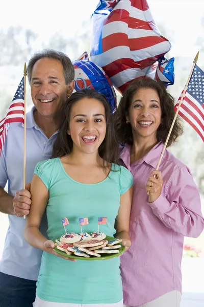 Семья на открытом воздухе на четвертое июля с флагами и печеньем улыбаясь Лицензионные Стоковые Изображения