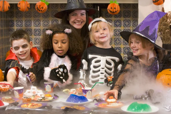 Four young friends and a woman at Halloween eating treats and sm Royalty Free Stock Photos