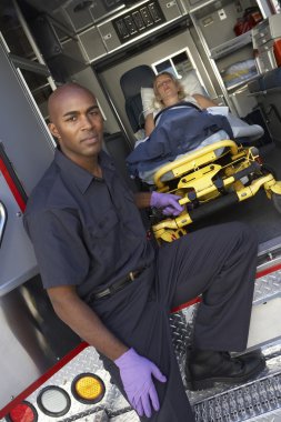 Male paramedic preparing to unload patient from ambulance clipart