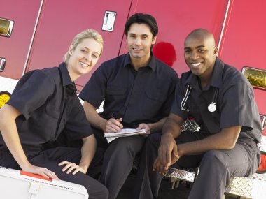 Three paramedics chatting and doing paperwork, sitting by their clipart