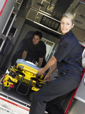 Two paramedics cheerfully removing empty gurney from ambulance clipart