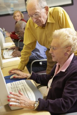 Senior man helping senior woman to use computer clipart