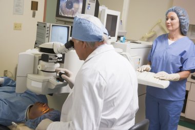 Doctor Checking Patient's Eyes With Nurse Assisting clipart