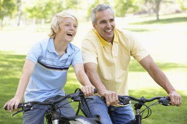 Father And Son Cycling Through A Park clipart