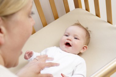 Mother Playing With Baby In Cot clipart