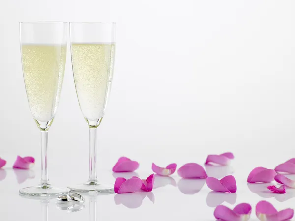 Twee trouwringen naast champagne fluiten en rozenblaadjes — Stockfoto