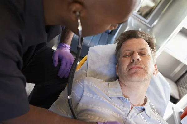 A mentősök sztetoszkóppal kezelik a beteget a mentőben — Stock Fotó