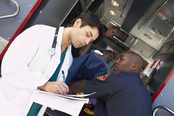 Hospital doctor taking notes as paramedics arrive with patient — Stock Photo, Image