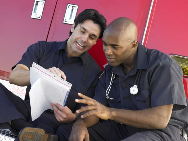 Two paramedics cheerfully doing paperwork, sitting by their ambu — Stock Photo, Image