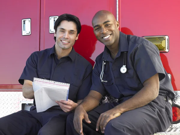Zwei Sanitäter, die munter Papierkram erledigen, neben ihrem Ambulanzwagen sitzend — Stockfoto
