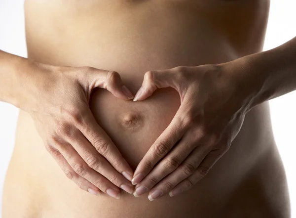 Detalle de la mujer embarazada que forma la forma del corazón con las manos — Foto de Stock