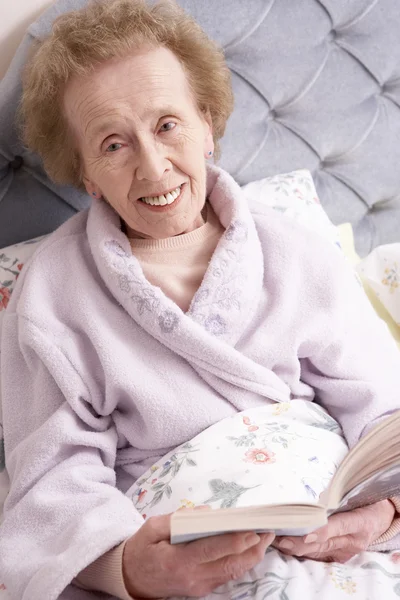 Senior vrouw ontspannen in bed met boek — Stockfoto