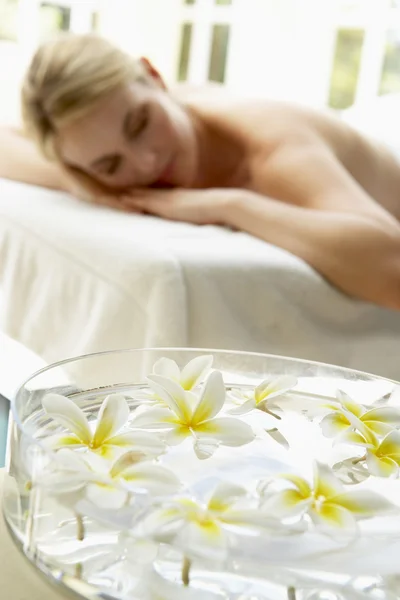 Kobieta na stół do masażu z kwiatami w planie — Zdjęcie stockowe