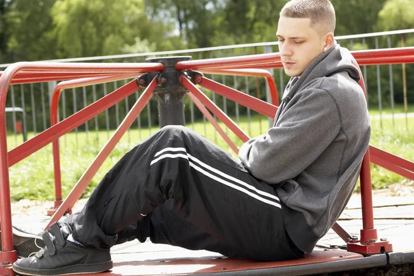 Junger Mann sitzt auf Spielplatz — Stockfoto
