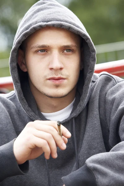 遊び場の喫煙の関節に座っている若い男 — ストック写真