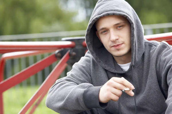 Junger Mann sitzt auf Spielplatz und raucht Joint — Stockfoto