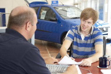 Young man filling in paperwork in car showroom clipart